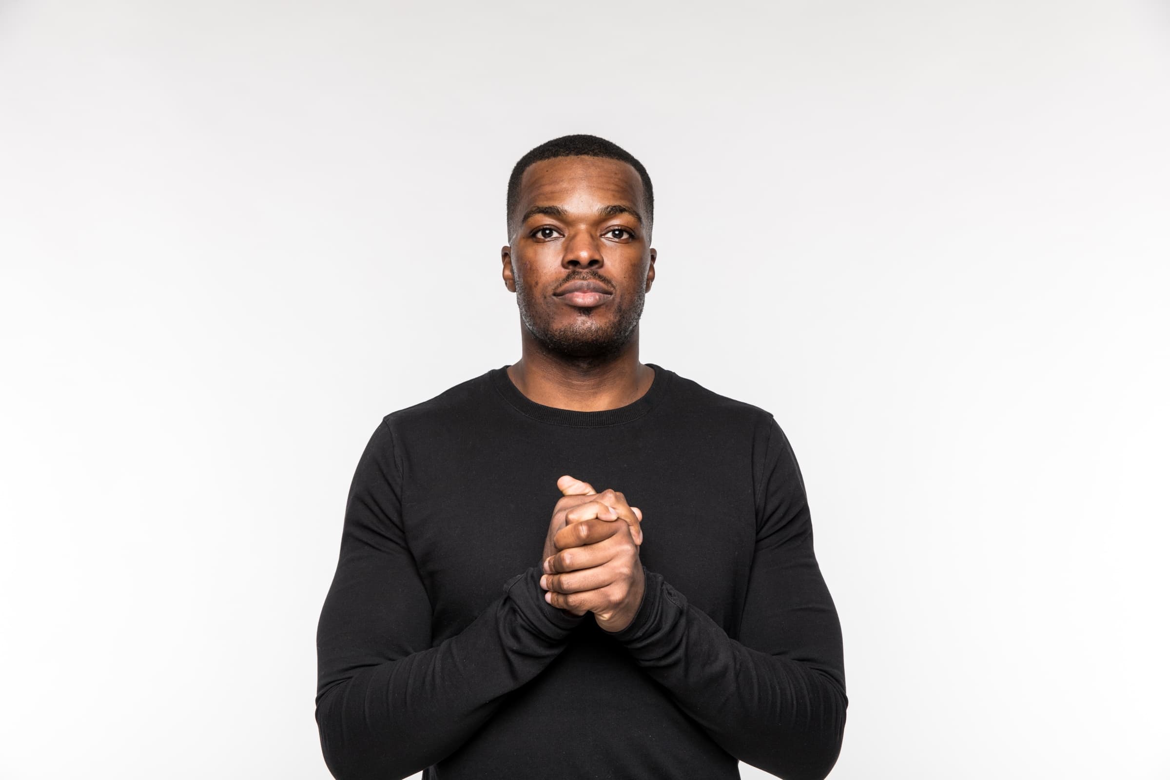 Akin, facing the camera in a black jumper, hands clasped